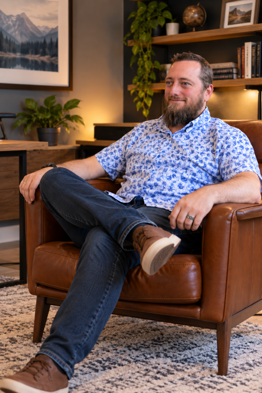 Joel Loughrin seated in a brown leather chair in his office, wearing a blue patterned shirt and jeans